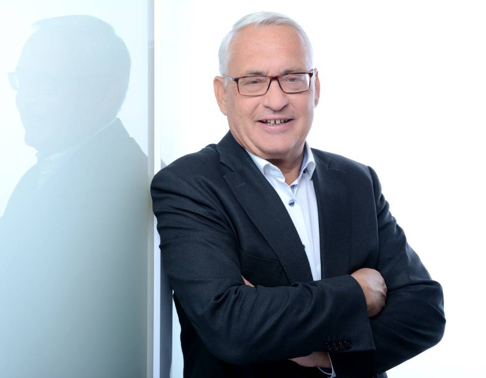 Mann mit Brille und verschränkten Armen vor spiegelnder Wand, Roger Tscheulin